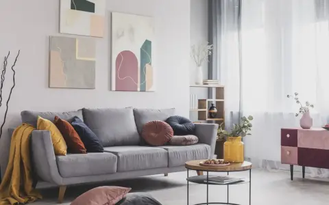 Divano grigio scuro con abbinamenti cuscini colorati e una coperta gialla. Tre quadri astratti decorano la parete.
