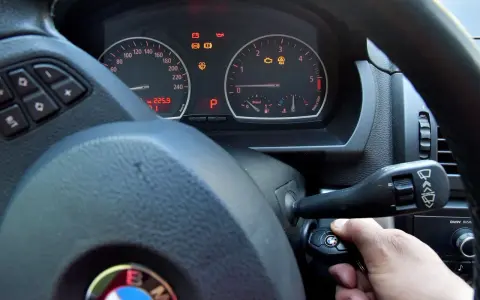 Ręka wsuwa kluczyk do stacyjki, by dowiedzieć się, jak odpalic auto. Na desce rozdzielczej świecą kontrolki.