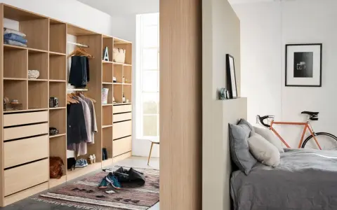 Un armario moderno y funcional, ideal para aprender como organizar un armario. Ropa colgada, cajones y estantes ordenados, con una bicicleta naranja y una cama al fondo.