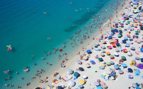 Spiaggia affollata con ombrelloni colorati e bagnanti nell'acqua cristallina, un'immagine perfetta per scoprire le località di mare più economiche in Italia.
