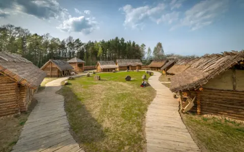 Drewniana osada średniowieczna Sławutowo z chatami krytymi strzechą, kamieniami i ścieżkami.