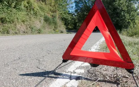 Czerwony trójkąt ostrzegawczy odległości stoi na poboczu drogi, sygnalizując awarię.