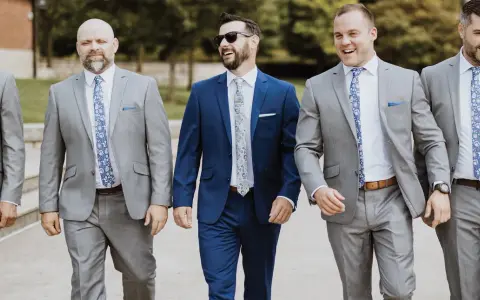 Groomsmen in grey suits and patterned ties walk together, showcasing stylish wedding pocket square folds.