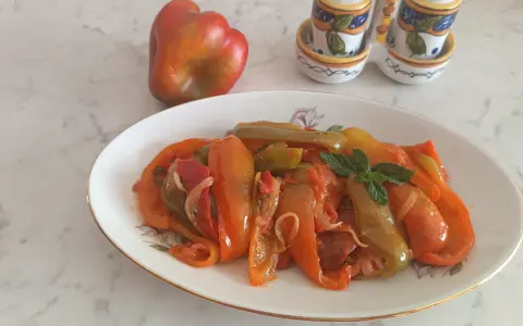 Piatto di peperoni alla siciliana, colorati e saporiti, con un peperone crudo sullo sfondo e saliere decorate.