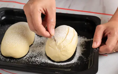 Eine Hand schneidet mit einem Messer Muster in ein mit Mehl bestäubtes Brot.