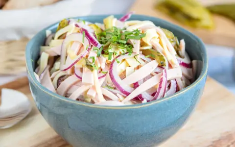 Schmackhafter schweizer wurstsalat mit roten Zwiebeln und Käse in einer blauen Schüssel, garniert mit Petersilie.