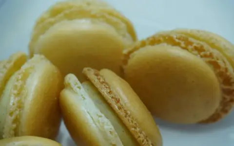 Macarons dorés à la ganache vanille, leurs coques délicates révèlent une garniture crémeuse et parfumée.
