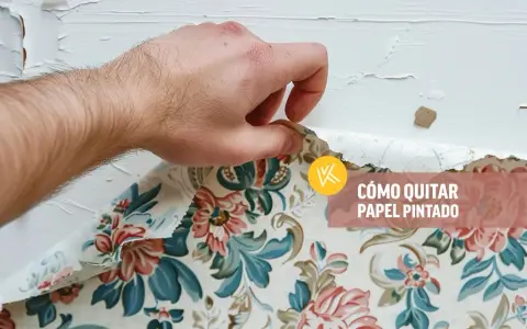Mano retirando papel pintado floral de una pared blanca.