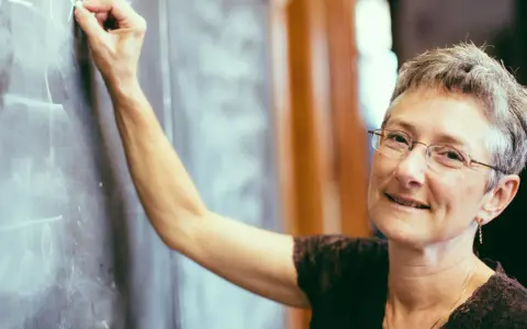 Lehrerin schreibt an Tafel. Was verdient ein Gymnasiallehrer? Sie lächelt wissend.