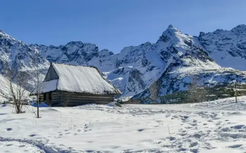 Zimowa hala Gąsienicowa. Drewniana chata kryta śniegiem, otoczona ośnieżonymi szczytami Tatr.