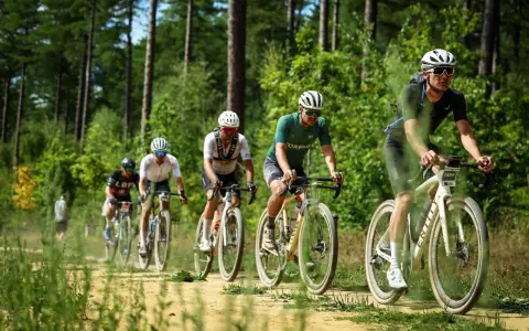 Radfahrer im Wald bei einem Gravel WM-Rennen. Staub wirbelt auf, während sie auf dem sandigen Weg fahren.