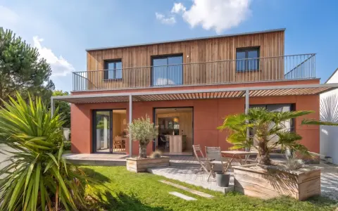 Maison moderne avec bardage bois et façade ocre. Idéal pour un conseil construction maison, avec jardin verdoyant et terrasse accueillante.