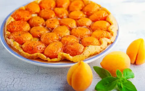 Découvrez les meilleures tartes aux fruits : une tarte tatin aux abricots dorés et caramélisés, garnie de fruits frais et de feuilles de basilic.
