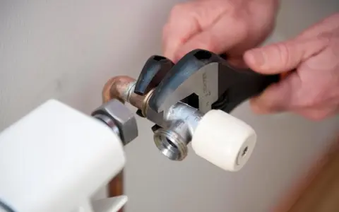 Manos ajustando llave de radiador con llave inglesa para cambiarla y evitar goteos.