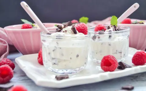 Zwei Gläschen mit cremigem Dessert, garniert mit Himbeeren und Schokostückchen. Ein köstliches Herrencreme Rezept zum Genießen.