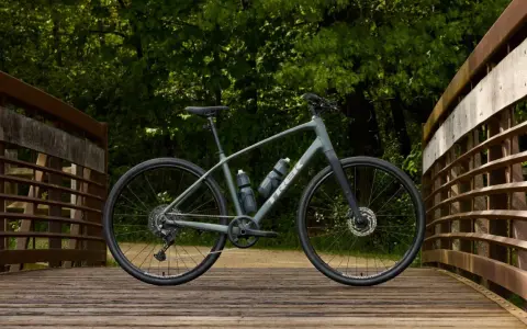 A grey Trek bike sits on a wooden bridge, ready for road or mountain biking adventures through the lush green forest.