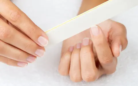 Une main lime délicatement ses ongles, comme un remède de grand-mère pour un ongle abîmé.
