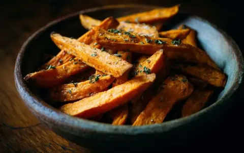 Un bol en bois rempli de frites de patate douce dorées et assaisonnées d'herbes.
