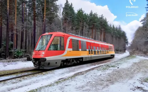 Czerwono-żółty pociąg EN 81-005 Polregio mknie przez zaśnieżony las.