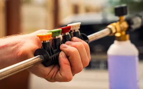 Choosing the right nozzle to pressure wash car is key. This hand holds a selection of colored tips for a pressure washer wand, ready for detailing.