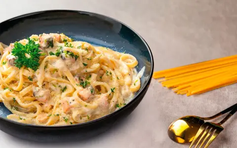 Pasta cremosa con trozos de salmón y perejil, servida en un plato azul oscuro.