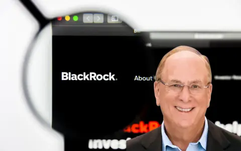 Uśmiechnięty mężczyzna w okularach, obok logo BlackRock. Larry Fink, jeden z założycieli BlackRock, na tle strony internetowej firmy.