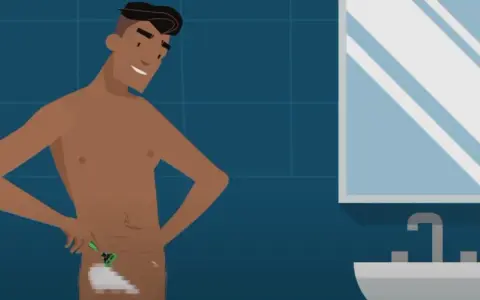 Hombre sonriente se afeita el vello púbico en el baño. Se ve su pene depilado.