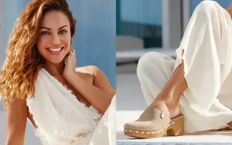 Mujer sonriente con vestido blanco y un pie calzado con zuecos de ante beige, adornados con tachuelas.