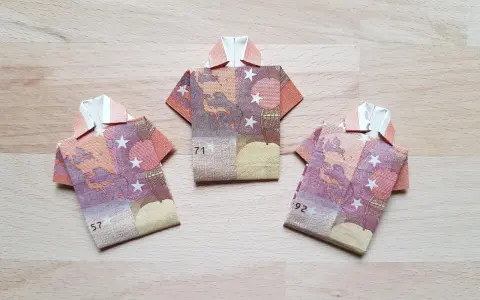 Drei gefaltete Euro-Scheine in Form von Hemden liegen auf einem Holztisch. Das kunstvolle Falten von Geld zu kleinen Hemden ist eine kreative Idee.