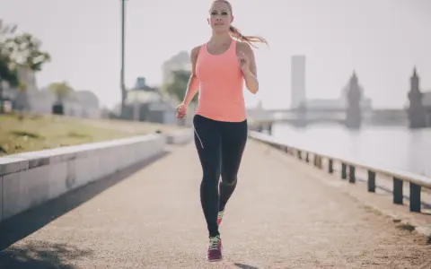 Frau joggt am Fluss entlang. Sie beweist, dass ist joggen gesund und ein toller Start in den Tag.