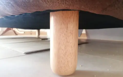 Una pata de madera de un canapé, mostrando cómo levantar un canapé del suelo para limpiarlo o moverlo.