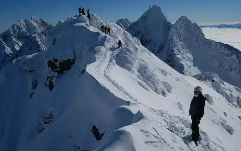 Zimowy trekking po graniach Tatr, gdzie śnieg tworzy prawdziwą koronę gór polskich. W oddali widać morze chmur.