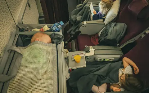 Niemowlę w samolocie śpi w gondoli, podczas gdy starsze dzieci oglądają bajki.