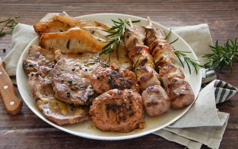 Un piatto invitante di grigliata di carne: costine, spiedini, salsicce e hamburger, guarniti con rosmarino fresco.