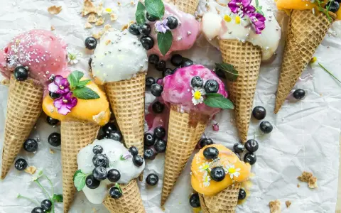 Bunte Eistüten mit Blaubeeren und Blüten. Wer fragt sich, wie viel Kalorien hat eine Kugel Eis, wenn sie so verlockend aussieht?