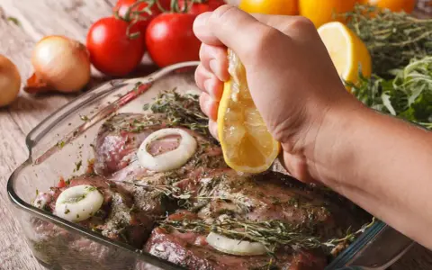 Fleisch marinieren für den Grill: Zitrone über mariniertes Fleisch mit Zwiebeln und Kräutern ausdrücken.