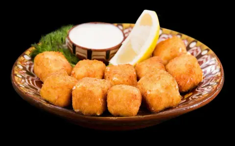 Croccanti cubetti di ricotta fritta salentina dorati, serviti su un piatto decorato con limone, salsa bianca e aneto.