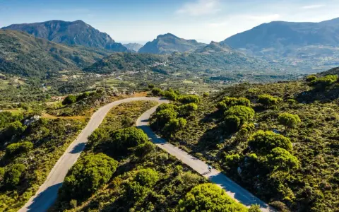 Ein Rennradfahrer auf Kreta genießt die kurvenreiche Straße durch eine grüne Berglandschaft.