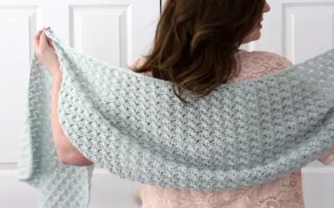 Mujer con chal rectangular de crochet azul claro sobre vestido rosa.