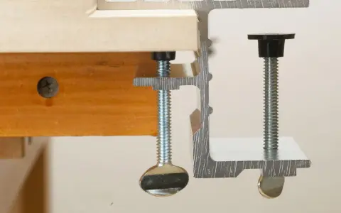 Dos tipos de abrazaderas metálicas sujetan una tabla de madera.