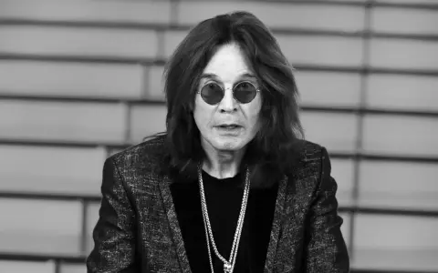Ozzy Osbourne w okularach i błyszczącej marynarce, z naszyjnikami. Plotki o tym, że Ozzy Osbourne nie żyje, są fałszywe.