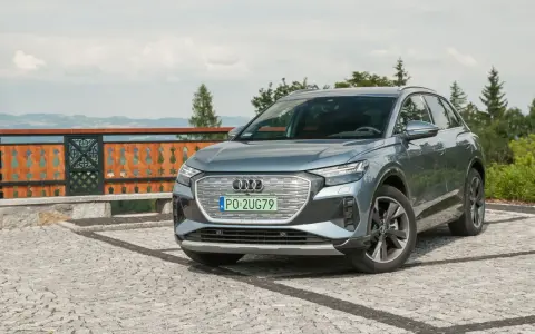 Szary Audi Q4 na kamienistym podjeździe, z widokiem na góry i las.