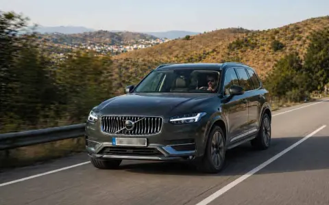 Volvo XC90 oscuro, uno de los suv mas fiables, circulando por una carretera rural con colinas verdes de fondo.