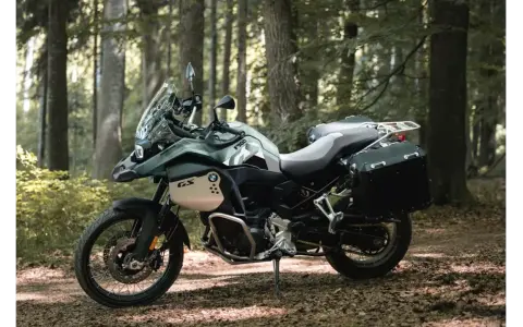 Zielony motocykl BMW F900GS z kuframi, gotowy na przygodę w lesie.