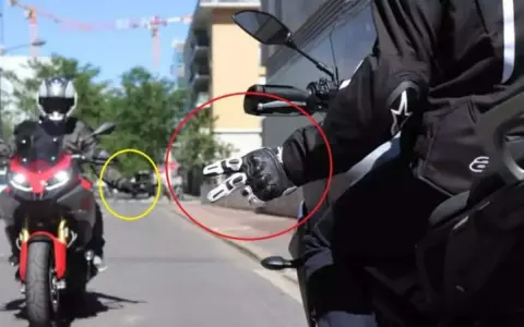 Mano guantata che fa il segno di pace, un gesto del linguaggio motociclisti. Un'altra moto in lontananza.