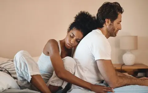 Un couple assis dos à dos sur un lit, l'air distant. On ne peut plus se parler sans s'engueuler.