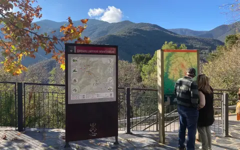 Pareja observa mapa de senderismo en los valles oriental de Montseny. El paisaje montañoso y el follaje otoñal crean un entorno pintoresco.