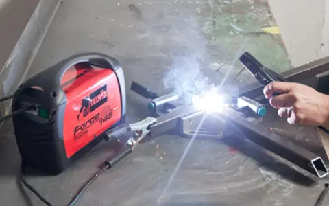Saldare fili sottili con una saldatrice Telwin Force 145. Scintille luminose e fumo si alzano mentre un artigiano lavora.