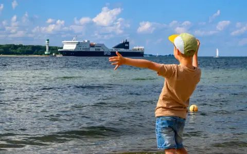 Kind winkt einem großen Schiff in Flensburg zu. Ein toller Ausflug mit Kindern, auch wenn es mal regnet.