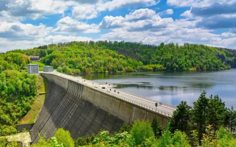 Die Talsperre im Harz staut einen See, umgeben von grünen Wäldern unter einem blauen Himmel mit weißen Wolken.